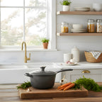 Gray cast iron cookware on a wooden cutting board with carrots and herbs in a bright kitchen.